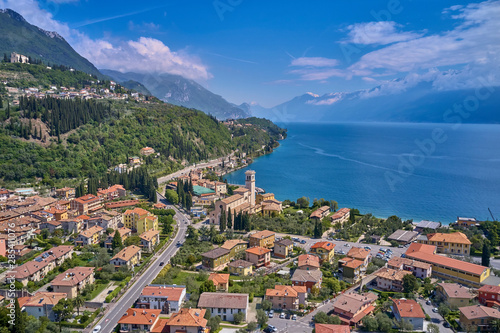 The resort town of Pulciano, located on the shores of Lake Garda. San Michele Arcangelo Church is located on a mountain. Panoramic view of the city, church, Lake Garda, Alps. Aerial view. © Berg