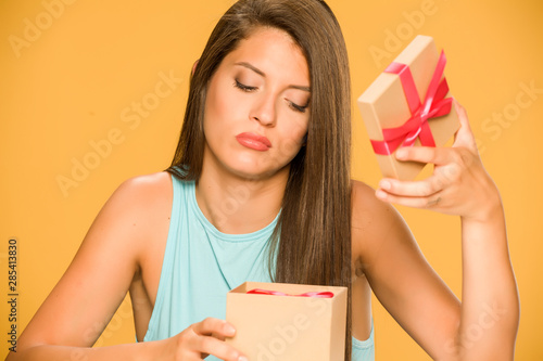 Young disappointed woman opening a present box on yellow background