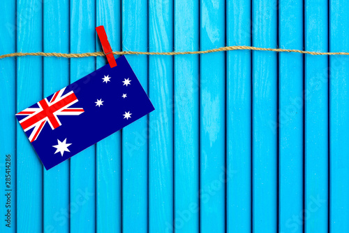 Flag of Australia hanging on clothesline attached with wooden clothespins on aqua blue wooden background. National day concept. photo