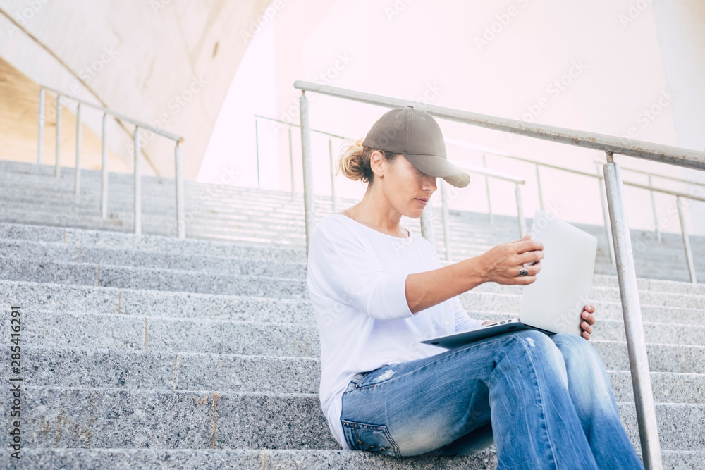 alone woman sitting on stairs with cap looking and working with her laptop or computer in serenity in the city - urban concept and buisness woman in silence