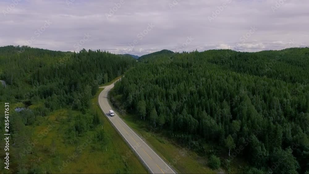 Aerial of white car driving on asphalt road in beautiful Norwegian forest nature Aerial of white car driving on asphalt road in beautiful Norwegian forest nature