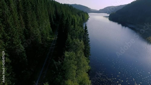 Aerial of dirt road running parallel with lake in beautiful Norwegian landscape