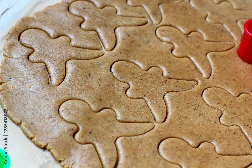 process of dealing with gingerbread man cookies,use red gingerbread man mold cutting gingerbread dough on baking paper around colorful cookie cutters on white wooden table.top view process of dealing with gingerbread man cookies,use red gingerbread man mold cutting gingerbread dough on baking paper around colorful cookie cutters on white wooden table.top view