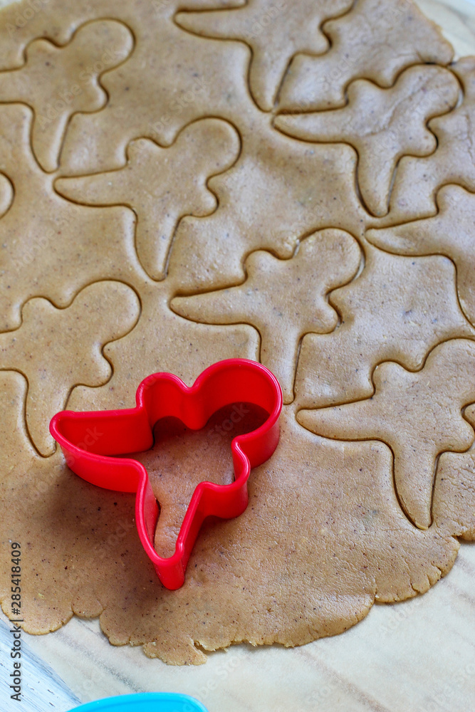 process of dealing with gingerbread man cookies,use red gingerbread man mold cutting gingerbread dough on baking paper around colorful cookie cutters on white wooden table.top view process of dealing with gingerbread man cookies,use red gingerbread man mold cutting gingerbread dough on baking paper around colorful cookie cutters on white wooden table.top view