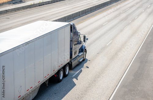 Dark big rig semi truck transporting cargo in dry van semi trailer running on wide multiline highway road photo