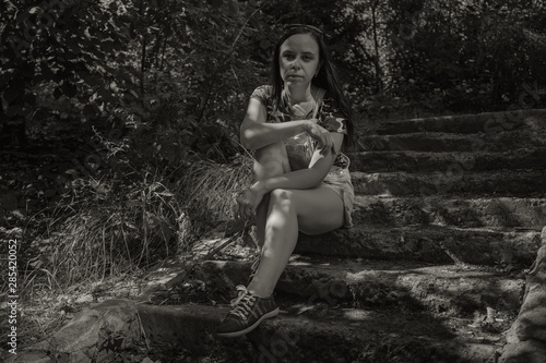 Sad woman sitting on the old steps in the Park  in black and white treatment. Female in sorrow