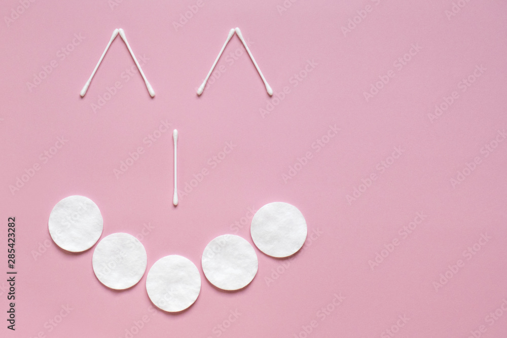 Flatlay white cotton buds and pads on pink with place for text. Face with a smile. Hygiene, medicine, health care, beauty concept Flatlay white cotton buds and pads on pink with place for text. Face with a smile. Hygiene, medicine, health care, beauty concept
