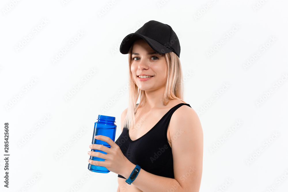 Young sporty blond woman in a black sportswear with smart watches holds bottle with water after workout standing over white background. Young sporty blond woman in a black sportswear with smart watches holds bottle with water after workout standing over white background.