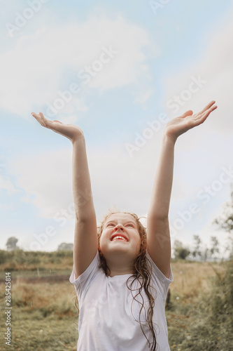 Laughing child spread its arms and catches raindrops and sunrayses.