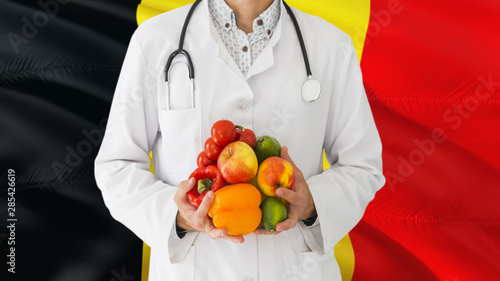 Belgian Doctor is holding fruits and vegetables in hands with Belgium flag background. National healthcare concept, medical theme.