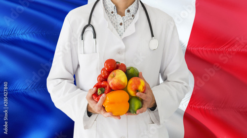 Doctor is holding fruits and vegetables in hands with France flag background. National healthcare concept, medical theme.