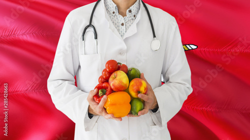 Doctor is holding fruits and vegetables in hands with Isle Of Man flag background. National healthcare concept, medical theme.