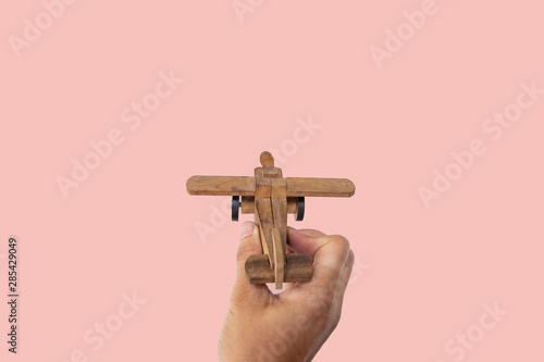 Hand holding wooden toy plane hand on pink background.