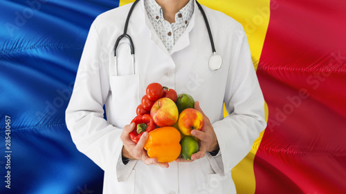 Doctor is holding fruits and vegetables in hands with Romania flag background. National healthcare concept, medical theme.