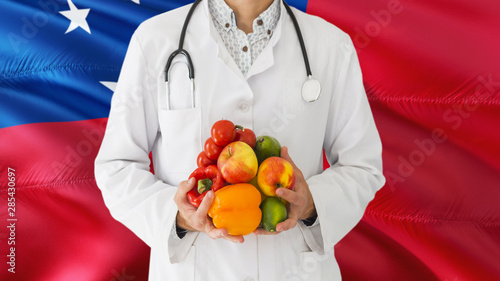 Doctor is holding fruits and vegetables in hands with Samoa flag background. National healthcare concept, medical theme.