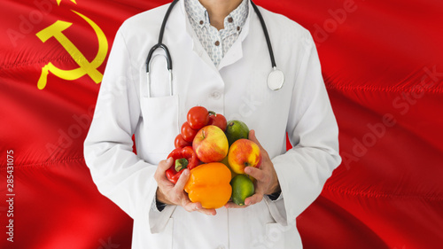 Doctor is holding fruits and vegetables in hands with Soviet Union flag background. National healthcare concept, medical theme.