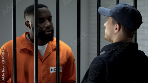 Obraz na plátně Afro-american prisoner making arrangement with prison guard, corruption in jail