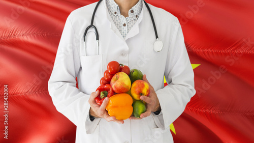 Doctor is holding fruits and vegetables in hands with Vietnam flag background. National healthcare concept, medical theme.