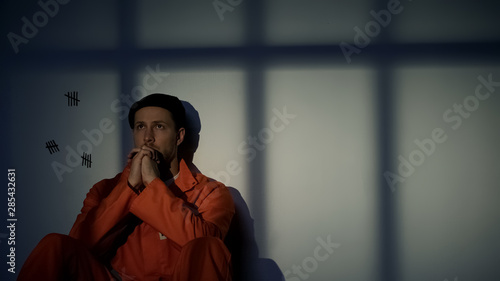 Caucasian male prisoner praying, feeling guilty about crimes, asking for mercy photo