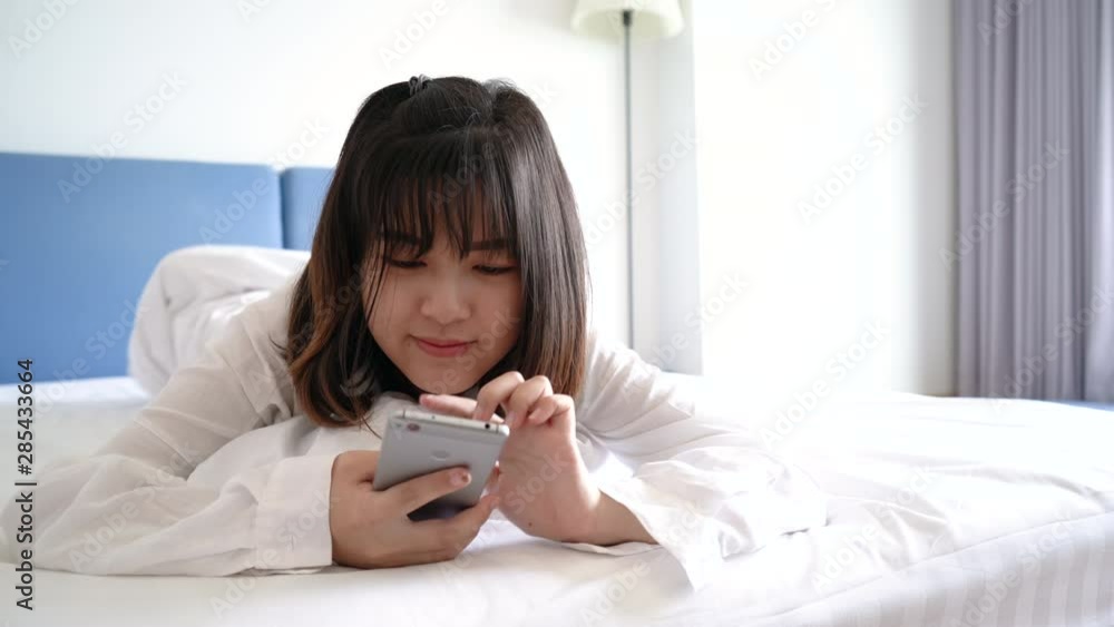 Beautiful Asian woman doing chatting with smartphone smiling happy on bed her lying under blanket in bedroom comfortable resting hotel people lifestyle Beautiful Asian woman doing chatting with smartphone smiling happy on bed her lying under blanket in bedroom comfortable resting hotel people lifestyle