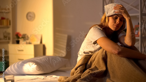 Sick lady with towel on forehead suffering from migraine, sitting in bed at home photo