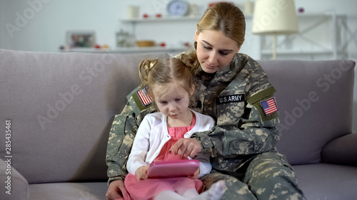 Military mother teaching little girl playing on toy tablet, educational gadget