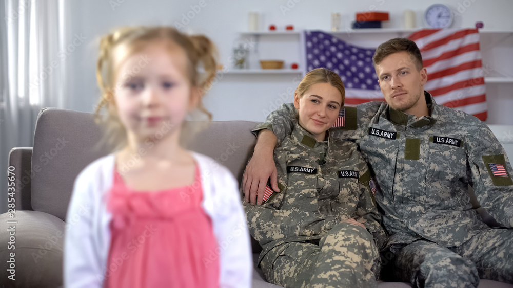 Fototapeta premium Joyful parents in US military uniform admiring little daughter looking at camera