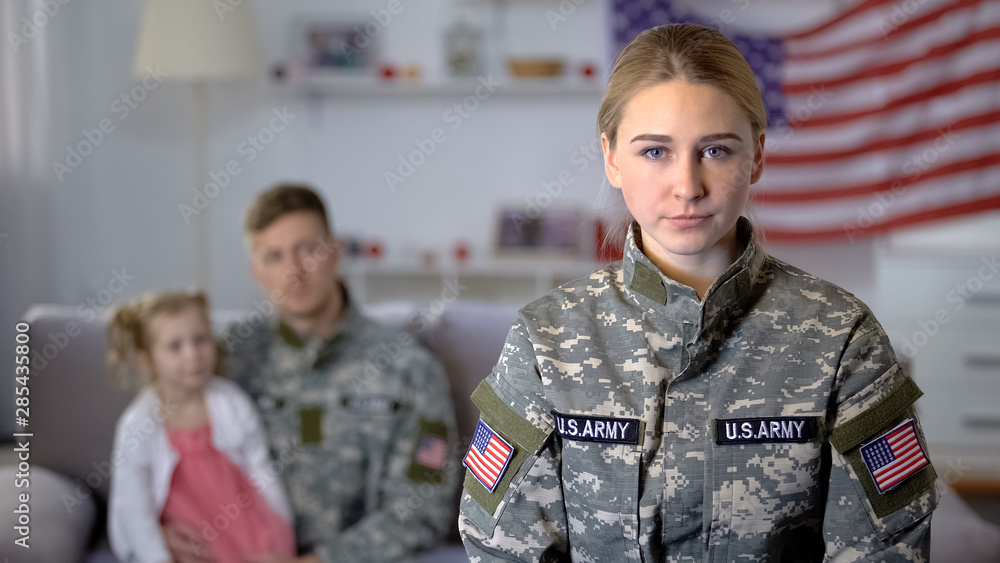 American military woman looking at camera, soldier husband and kid on background