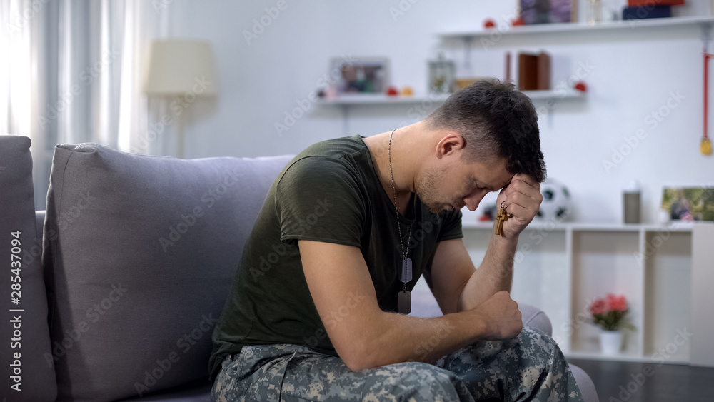 Male military praying, holding wooden cross in hand, remembering dead comrade Male military praying, holding wooden cross in hand, remembering dead comrade