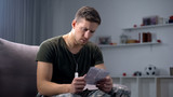 Troubled male soldier putting together parts of torn family photo, break-up