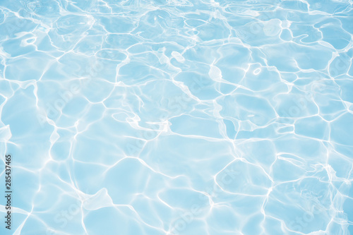 Blue water surface with bright sun light reflections in swimming pool background