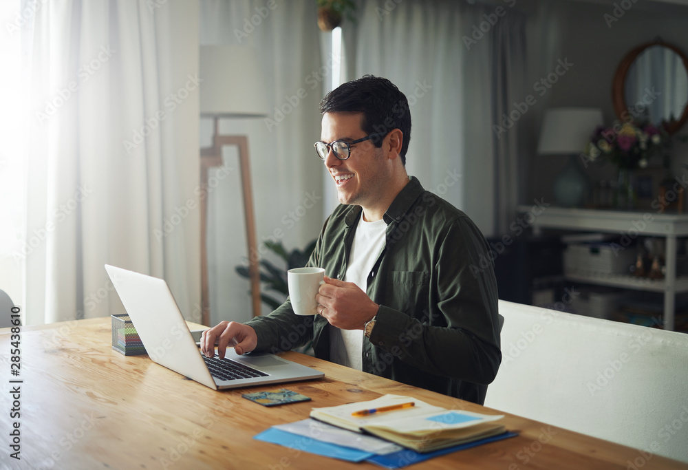 Smiling man enjoying the coffee while using laptop at home