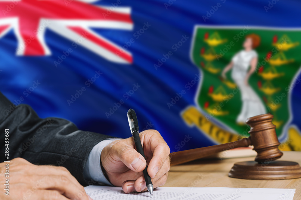 Judge writing on paper in courtroom with British Virgin Islands flag ...