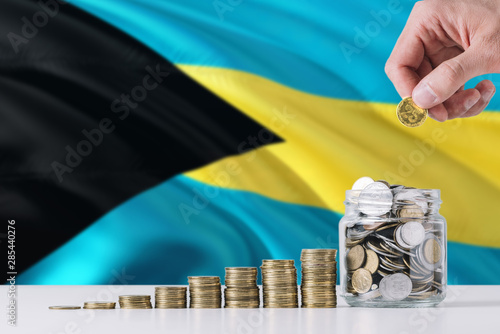 Business man holding coins putting in glass, Bahamas flag waving in the background. Finance and business concept. Saving money. photo