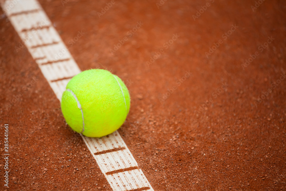 A yellow tennis ball lies on the clay court.