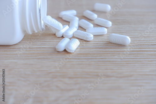 White medical pills spilling out of a drug bottle on a wooden backgrounds