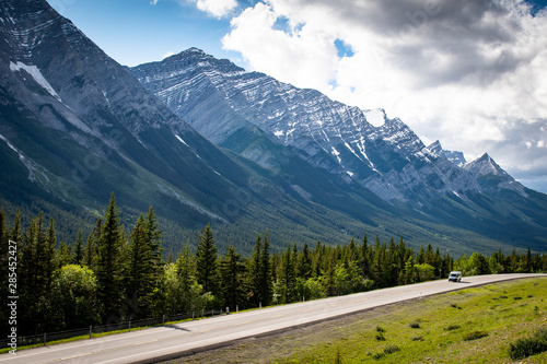 Road leading to Banff National Park in the Canadian Rockies, showing snow caps mountain peaks.