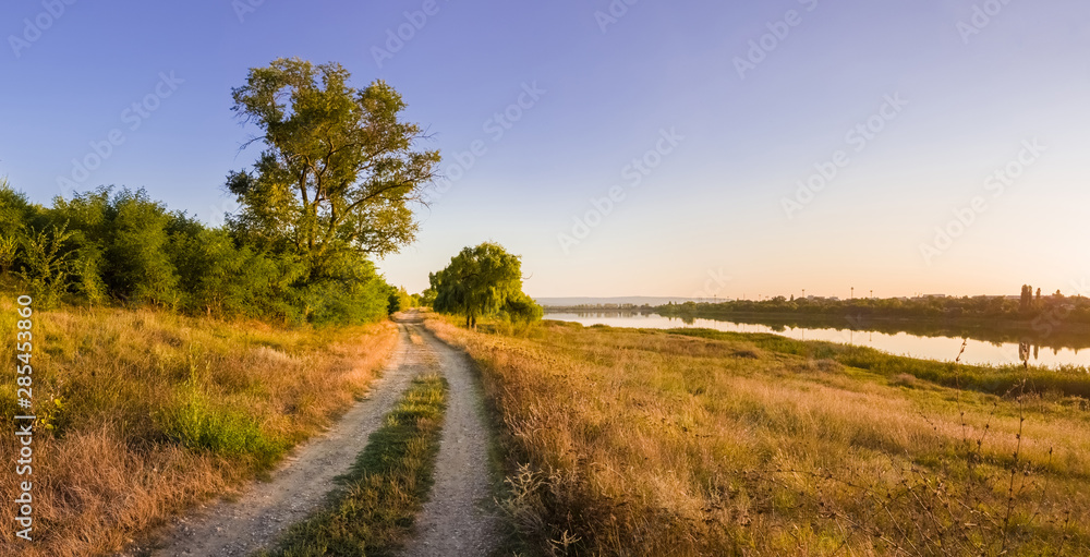 Fototapeta premium Scenic countryside landscape with rural dirt road across a meadow with dry grass and hay under a clear blue sky. Autumn panorama view near Delia lake, Ungheni, Moldova.