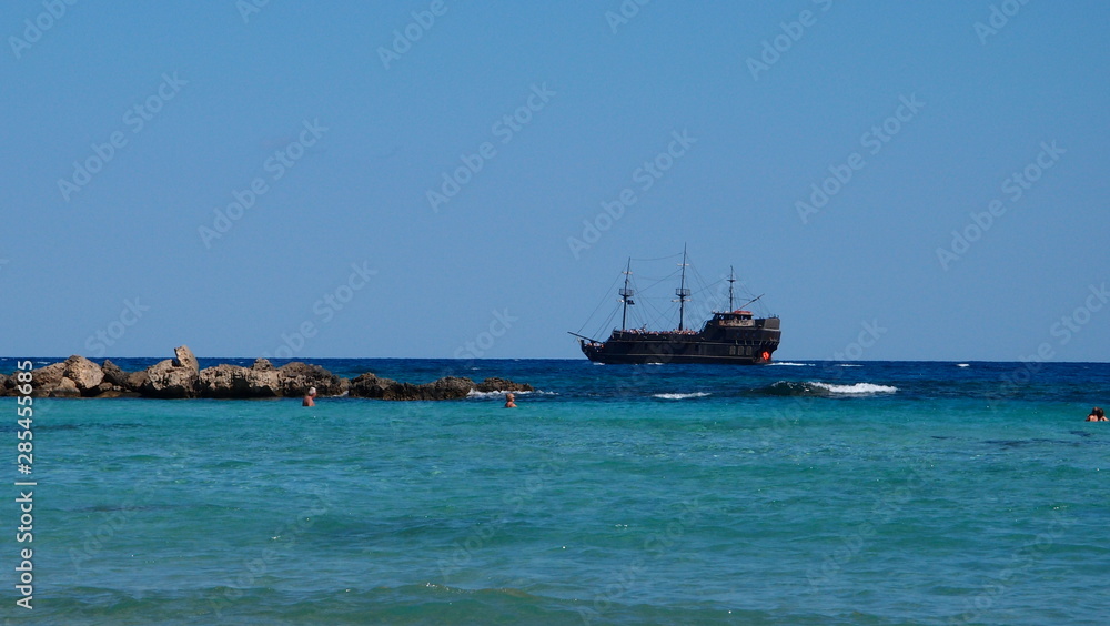Stylized as a pirate ship, floating in the turquoise blue sea with white lamb and rocks