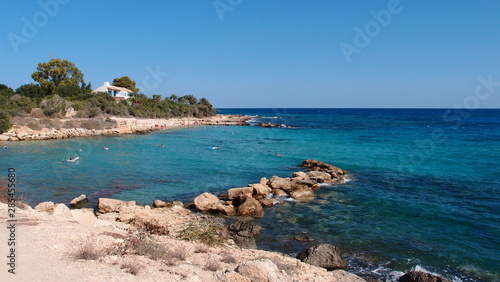 A small rocky spit forms a small bay with a warm transparent turquoise sea and stones at the bottom