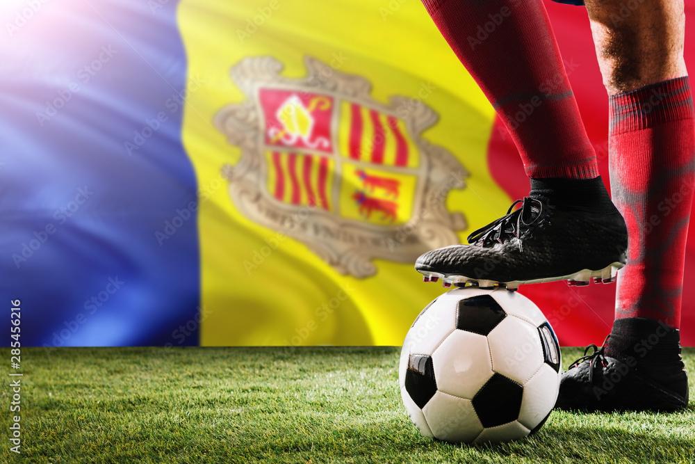 Close up legs of Andorra football team player in red socks, shoes on soccer ball at the free kick or penalty spot playing on grass.