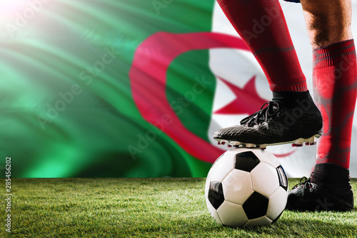 Close up legs of Algeria football team player in red socks, shoes on soccer ball at the free kick or penalty spot playing on grass.