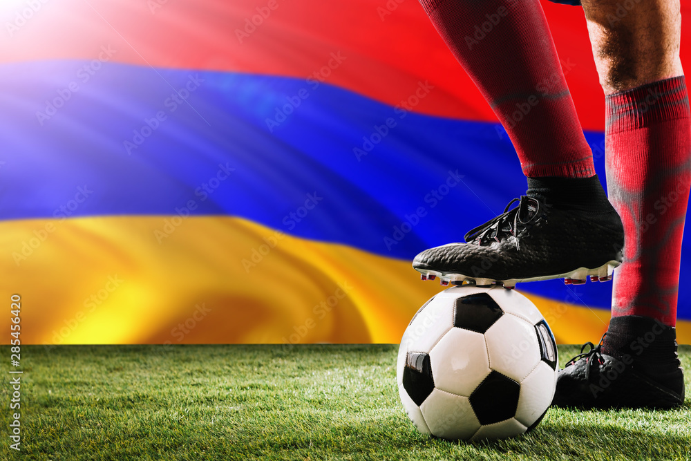 Close up legs of Armenia football team player in red socks, shoes on soccer ball at the free kick or penalty spot playing on grass.