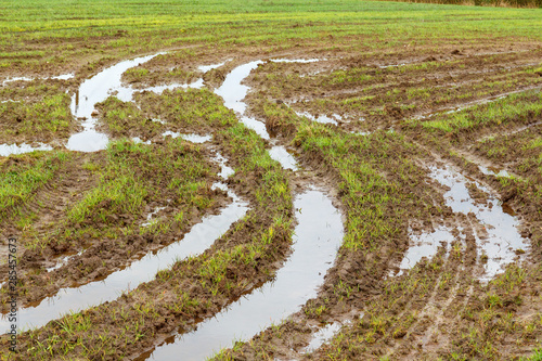 Field and road after heavy rains. Deep ruts from the wheels of agricultural machinery, puddles and dirt on the field. Severe weather conditions during field work due to rain in agriculture.