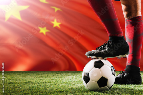 Close up legs of China football team player in red socks, shoes on soccer ball at the free kick or penalty spot playing on grass.