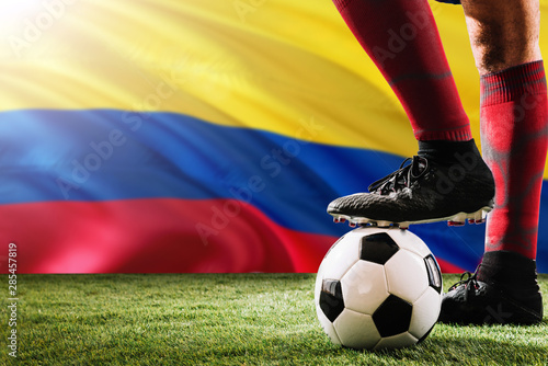 Close up legs of Colombia football team player in red socks, shoes on soccer ball at the free kick or penalty spot playing on grass.