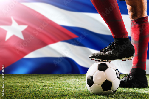 Close up legs of Cuba football team player in red socks, shoes on soccer ball at the free kick or penalty spot playing on grass.