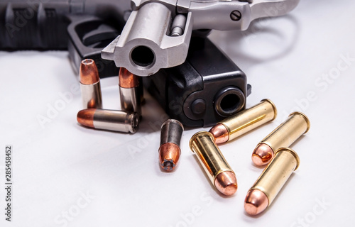 A snub nosed, stainless 357 magnum revolver on top of a black 9mm pistol with four bullets each caliber in front of them on a white background