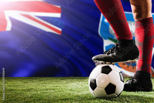 Close up legs of Falkland Islands football team player in red socks, shoes on soccer ball at the free kick or penalty spot playing on grass.