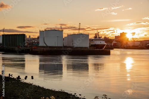Ship moored to a pier with oil tanks in a commercial harbour at sunset. Aberdeen, Scotland, UK